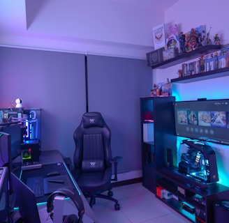 A modern gaming setup featuring a sleek gaming chair, dual monitors on a desk, and LED lighting. A gaming console and various decorations are displayed on shelves, creating an organized and vibrant gaming environment.