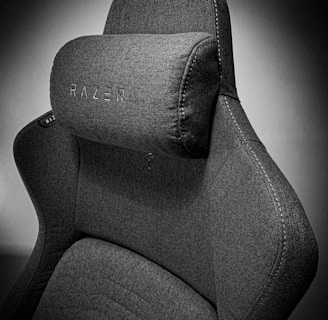 A high-quality, fabric gaming chair featuring ergonomic design and enhanced comfort. The chair has a distinct headrest with visible stitching, embossed branding, and a modern aesthetic.